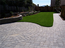 Enclosed back yard with path, patio and retainer wall made of gray pavers
